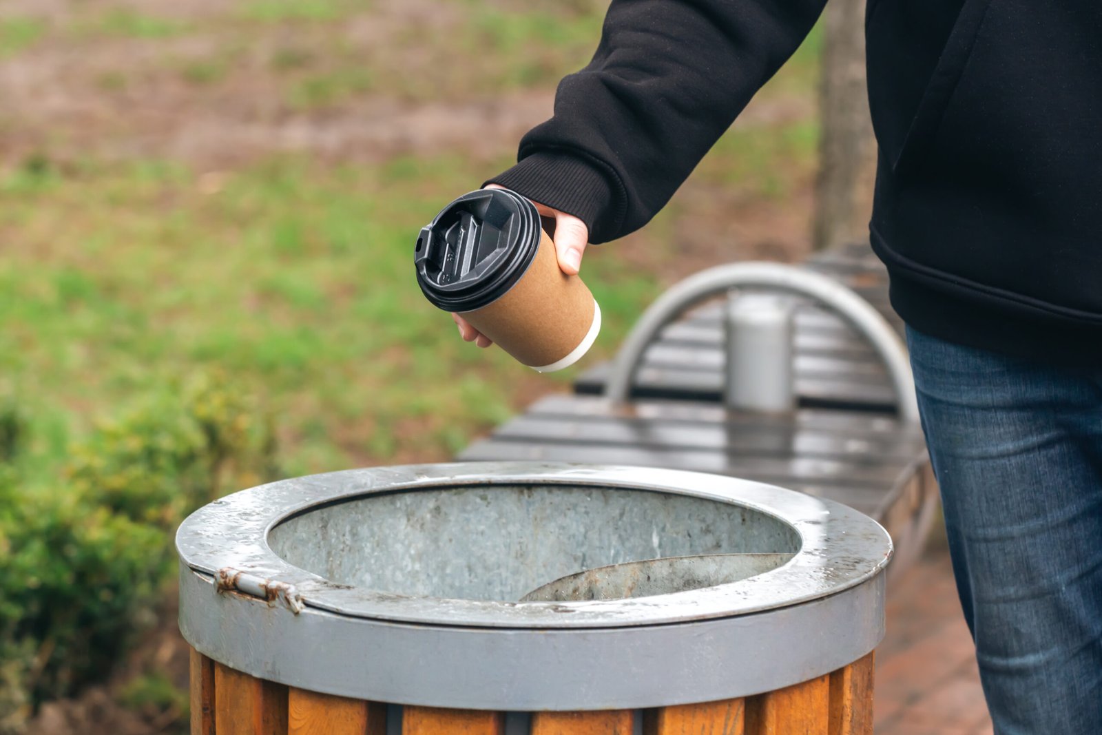 man throws paper disposable cup into trash can park scaled